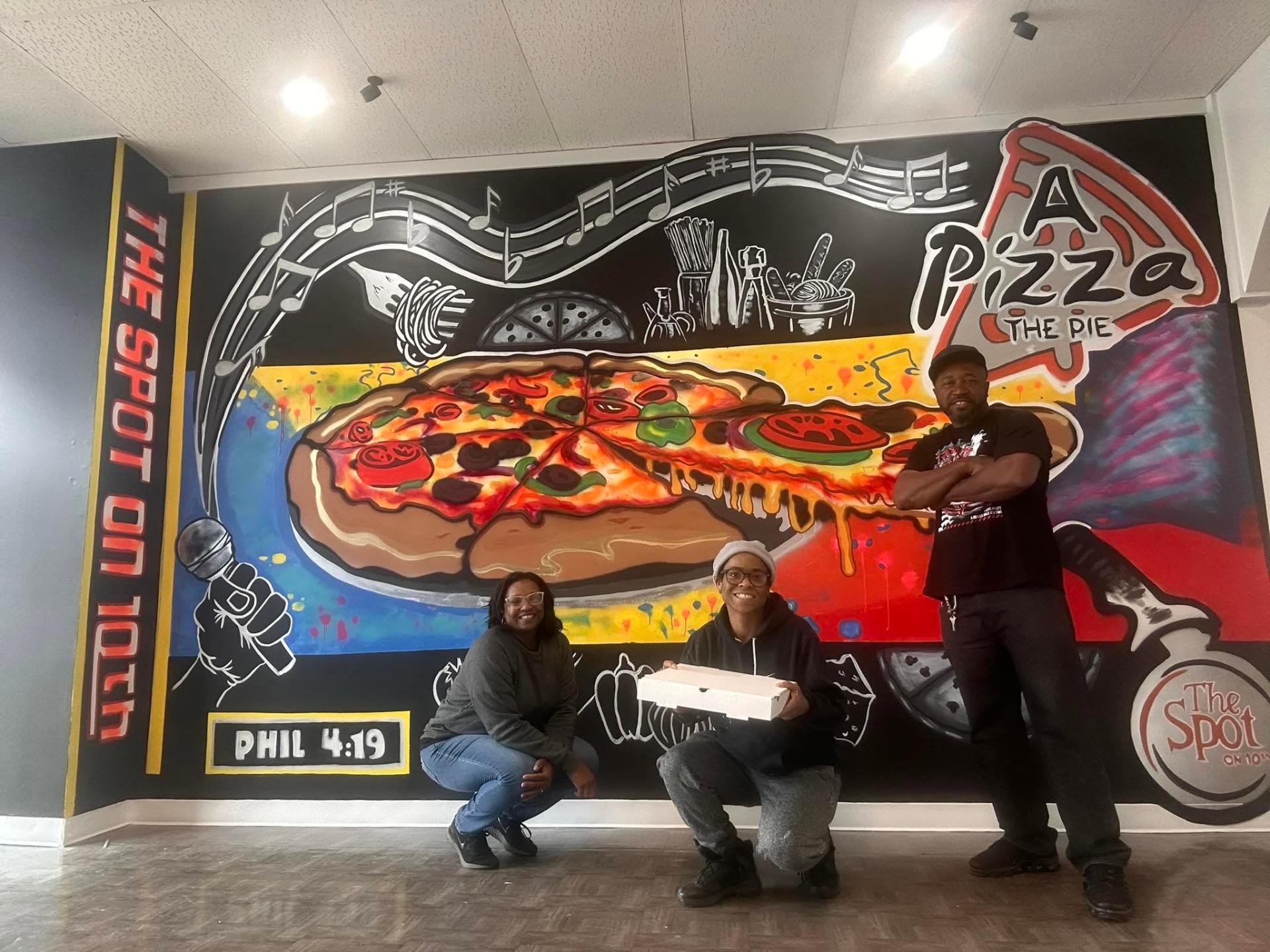 Customers posing in front of the pizza mural at The Spot on 10th