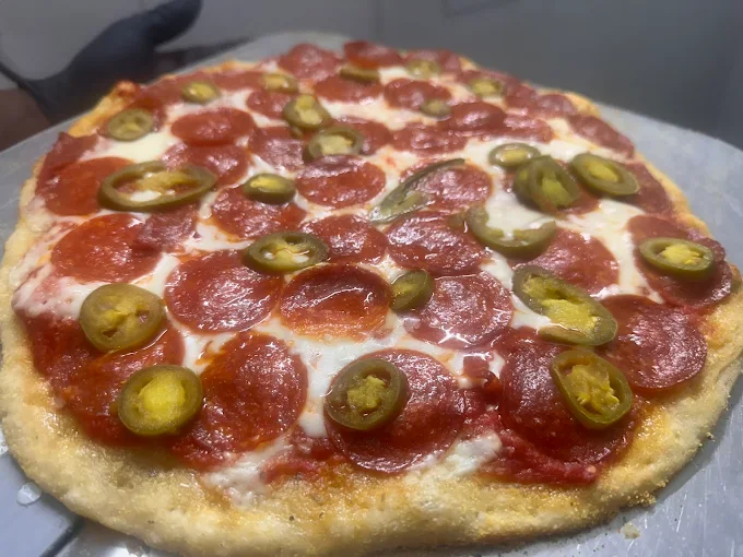 Fresh pepperoni and jalapeño pizza on a metal peel